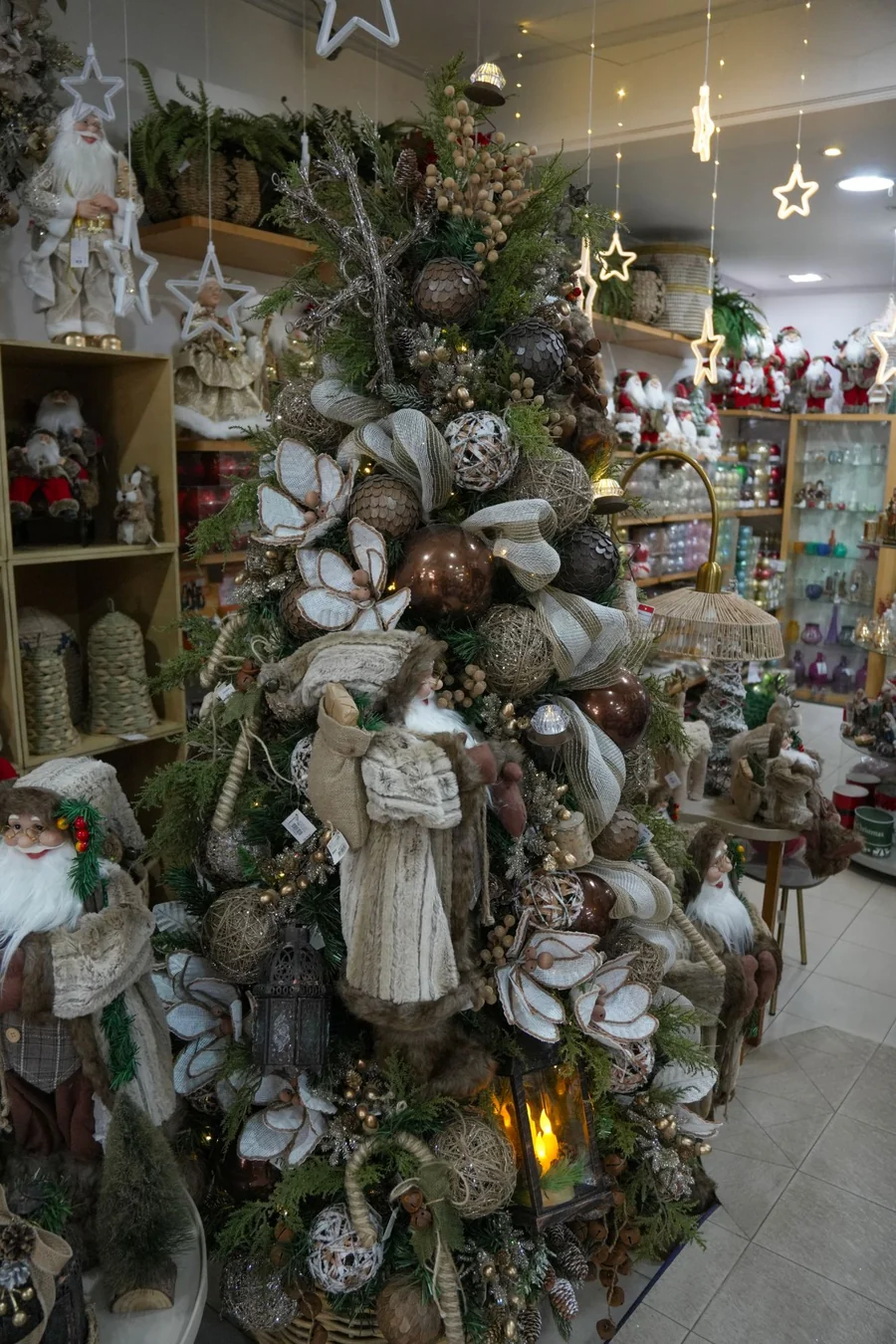 Árvore de Natal alta montada dentro do salão, em tons de palha e marrom, com laços de juta, bolas e papais-noéis em volta