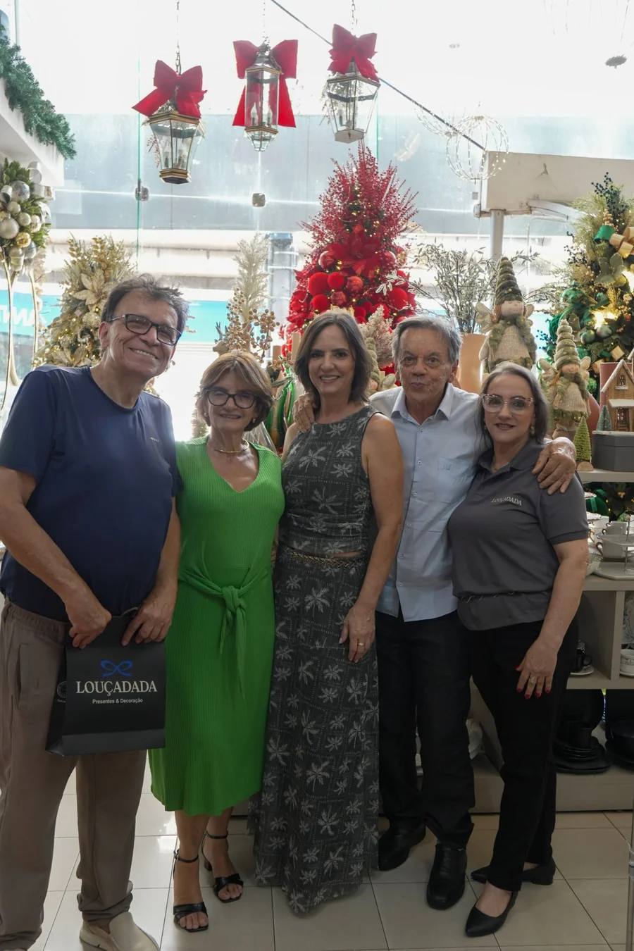 Cinco pessoas posando juntas diante da árvore vermelha montada na loja, uma delas com a sacola da Louçadada na mão