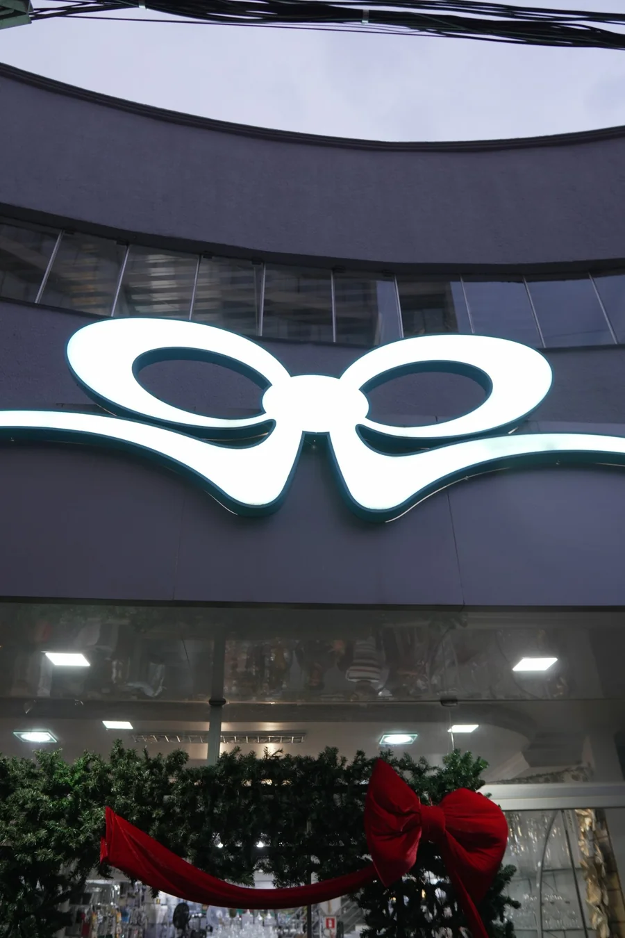 O laço da Louçadada, em escala monumental e iluminado por dentro, sobre a fachada da loja, visto de baixo