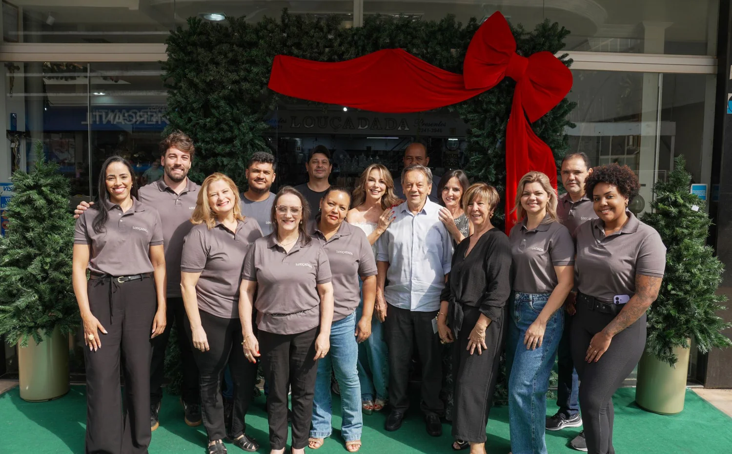 A equipe da Louçadada posada na calçada em frente à loja, de camisa cinza da casa, embaixo de uma guirlanda verde com laço vermelho que emoldura a porta
